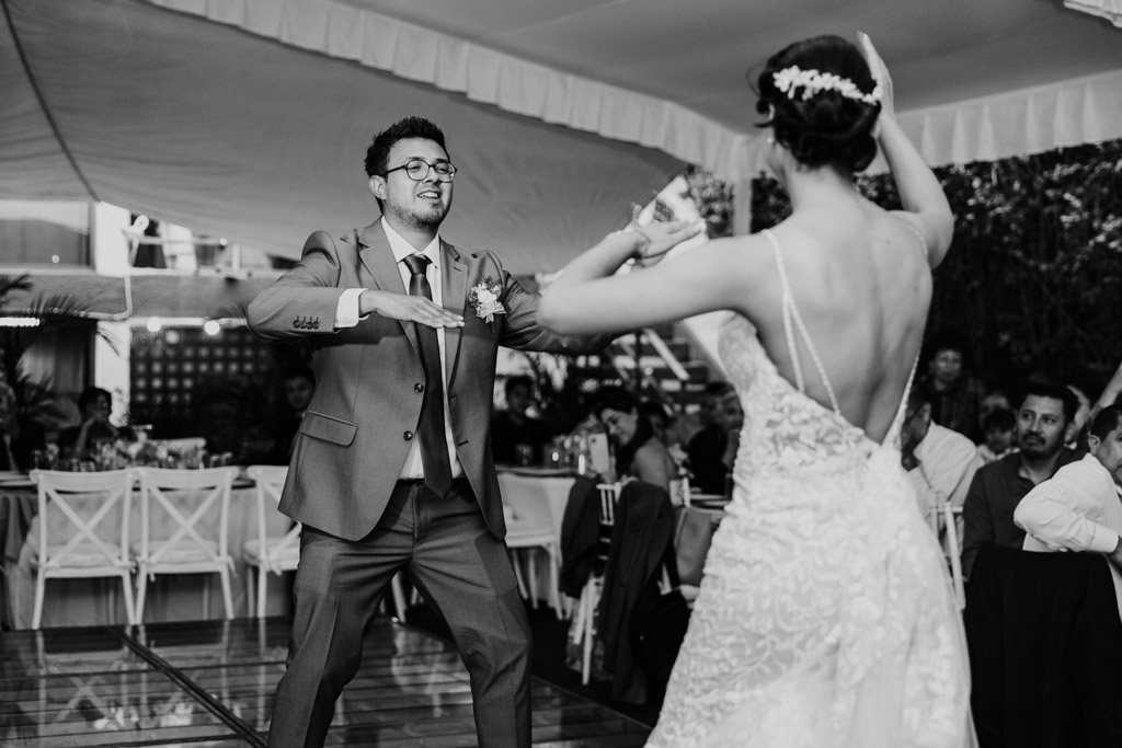 Black and white photo of bride and groom joyfully dancing together at their Mexico City wedding reception, surrounded by guests