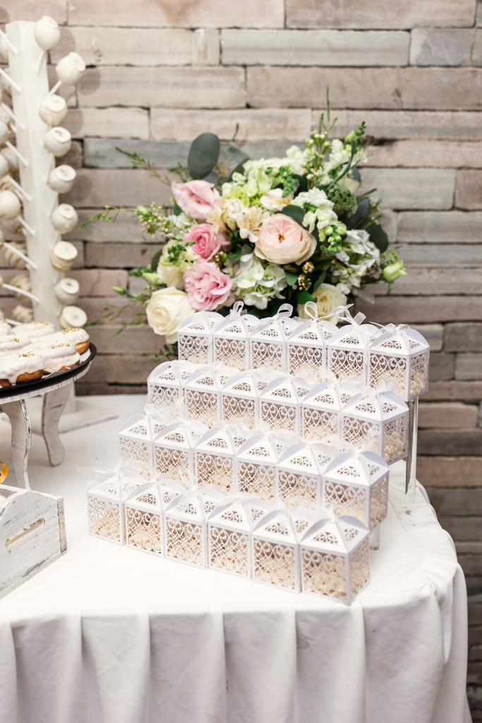 White decorative boxes stacked on dessert table with flowers in the background for Mexico City wedding reception