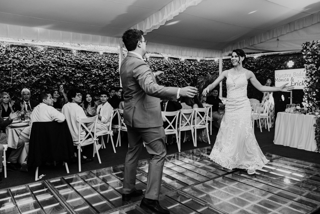 Black and white photo of bride and groom dancing together at their Mexico City wedding reception as guests watch and smile