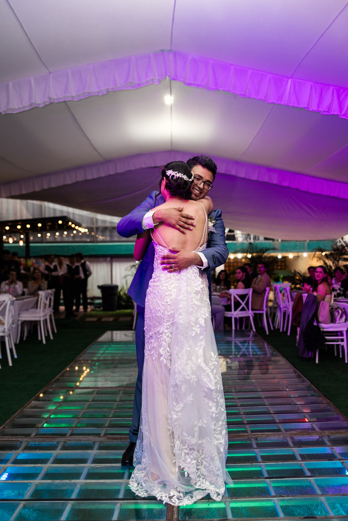 Bride and groom embrace during their first dance during Mexico City wedding reception under a tent with purple lighting