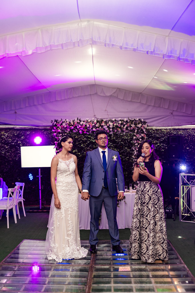 Bride and groom holding hands while a woman speaks into a microphone at their Mexico City wedding reception