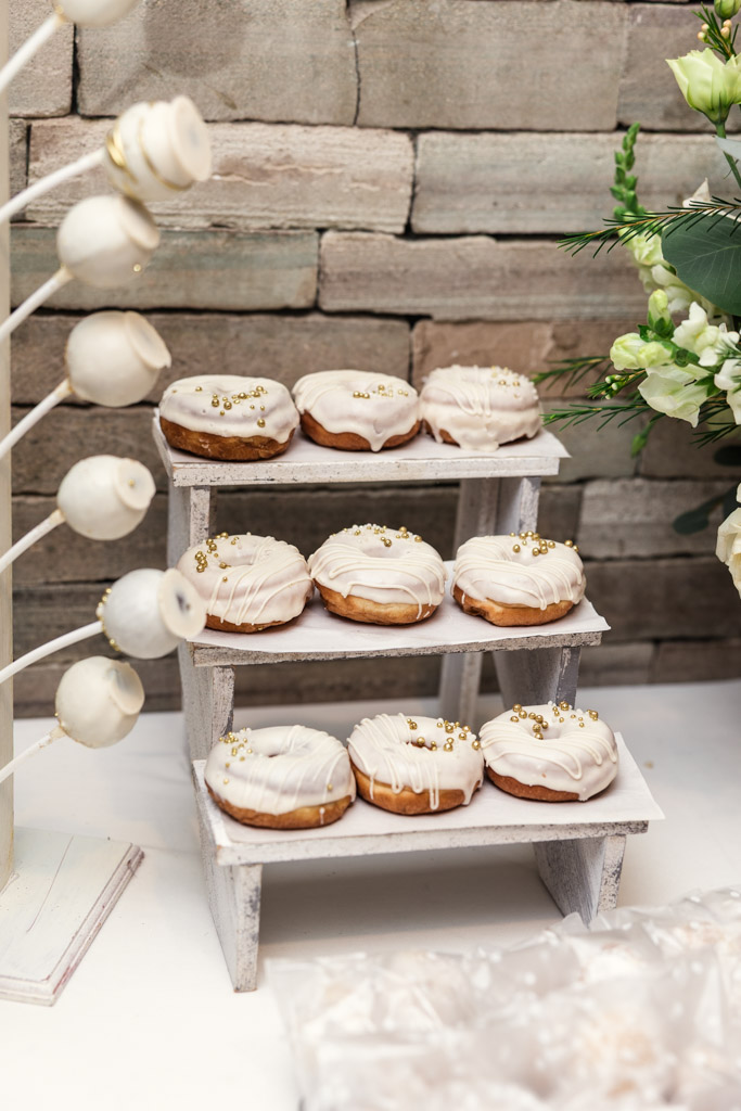Iced donuts with white drizzle and gold sprinkles displayed on a rustic stand, with cake pops on the side for Mexico City wedding reception