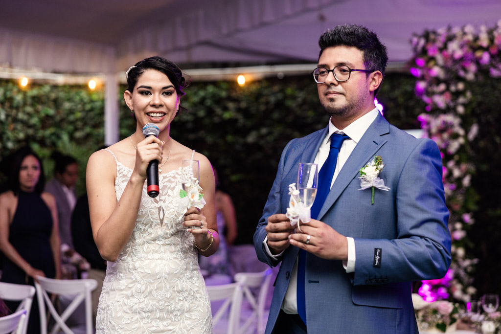 Bride gives a speech as she and groom hold glasses of champagne staning together at their vibrant Mexico City wedding reception