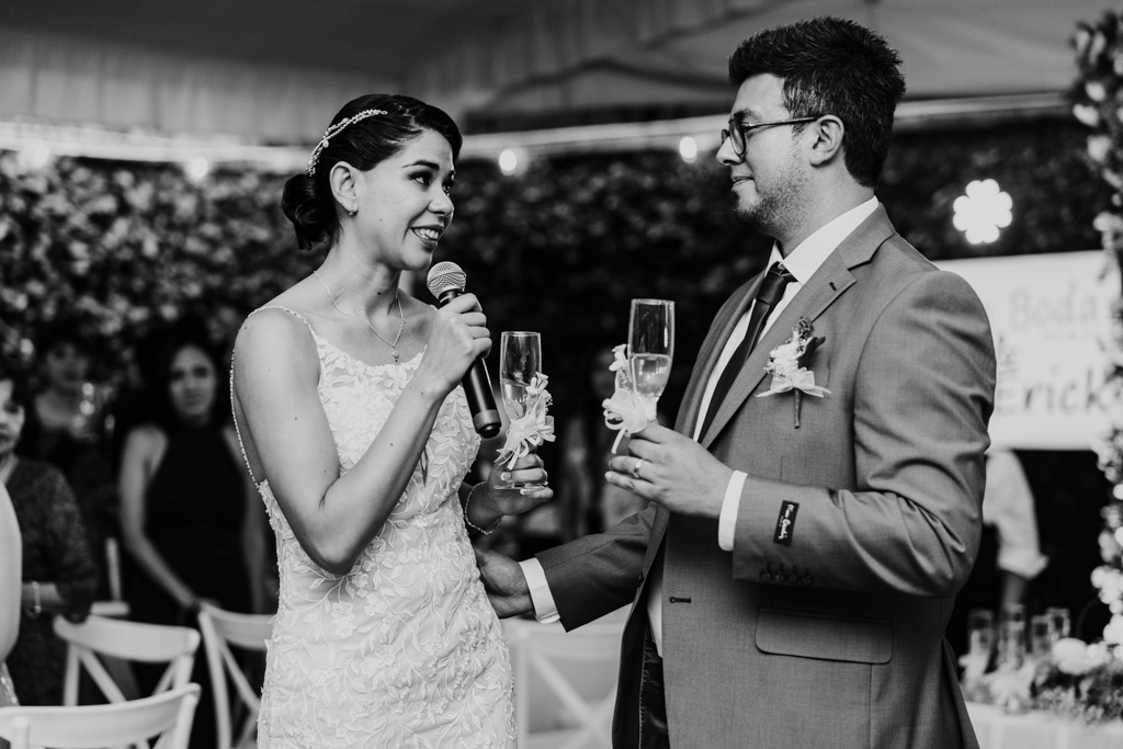 Black and white photo of bride and groom in formal attire giving a speech with champagne glasses at their Mexico City wedding reception