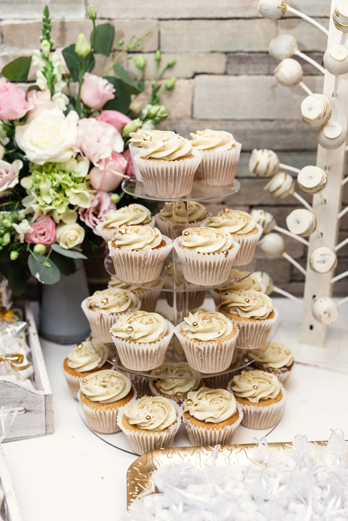 A tiered stand of cupcakes with frosting sits beside a bouquet of pink and white flowers on dessert table for Mexico City wedding reception