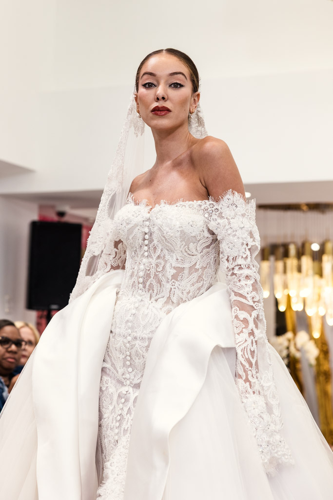 A woman models an elegant off-shoulder lace wedding dress with a veil at New York Bridal Fashion Week.