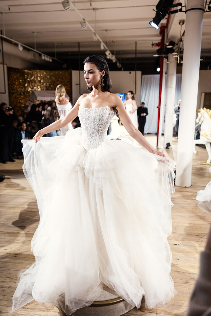 A model in a strapless white wedding gown poses on a wooden floor during New York Bridal Fashion Week.