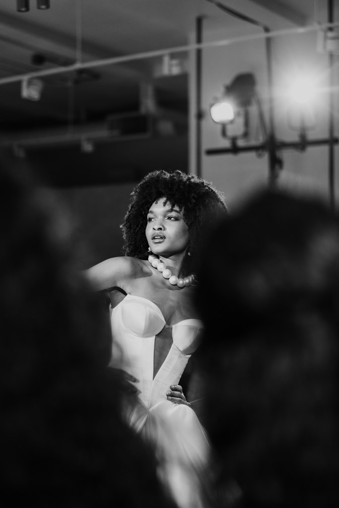 Black and white photo of a woman in a strapless dress and chunky necklace, elegantly posing on the runway at New York Bridal Fashion Week.