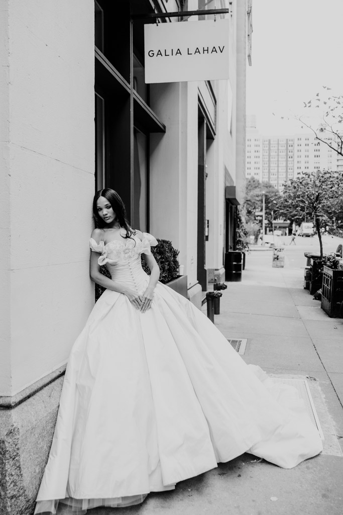 A woman in a ballgown wedding dress stands by a building under a