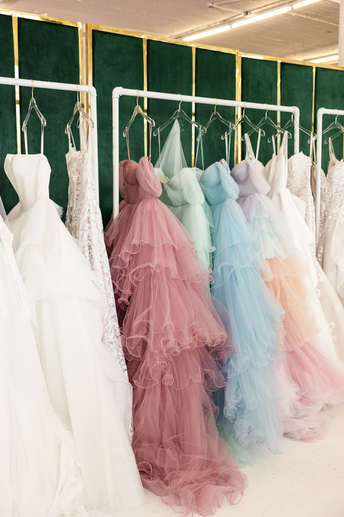 Colorful tulle gowns and white wedding dresses hang on racks in a boutique-style setting, inspired by trends from New York Bridal Fashion Week.