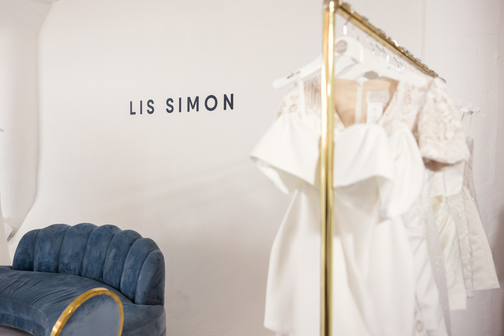 A rack of white dresses beside a blue velvet couch with
