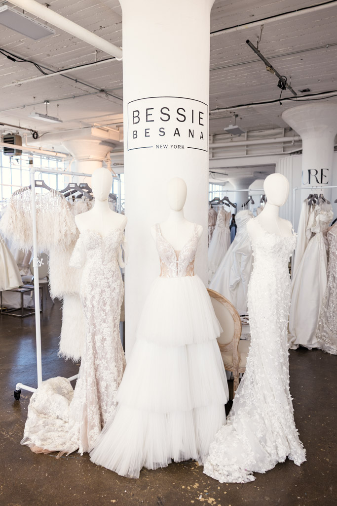 Three mannequins display elegant white wedding dresses in a bridal studio with a Bessie Besana sign, capturing the sophistication of New York Bridal Fashion Week.