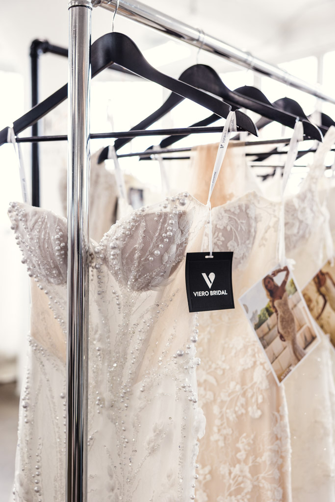 Close-up of elegant Viero Bridal wedding dresses with beaded details hanging on a rack, capturing the glamour of New York Bridal Fashion Week.
