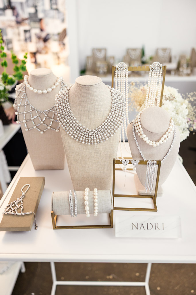Display of pearl and crystal jewelry on beige stands, with a sign reading
