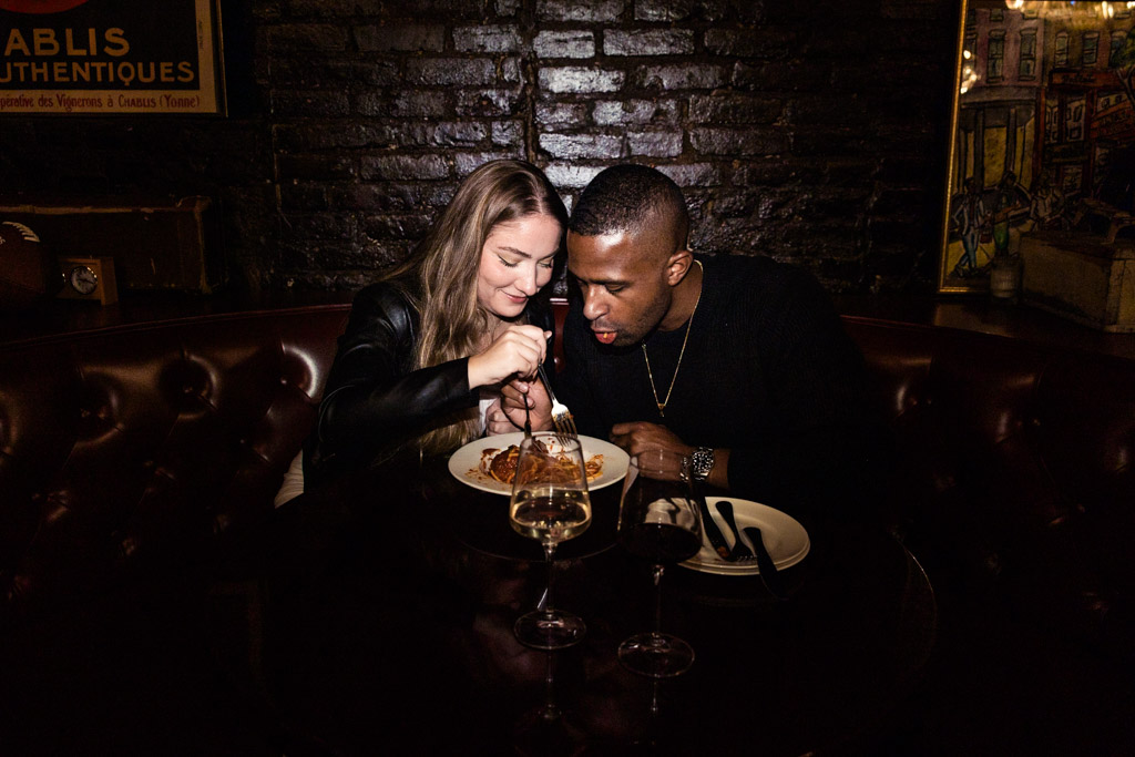 Engaged couple shares a plate of pasta at a dimly lit restaurant booth in Emilio's Ballato in New York City