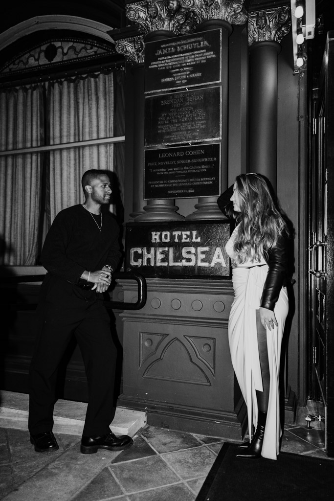 Candid photo of man and woman standing outside Hotel Chelsea at night during New York City engagement session