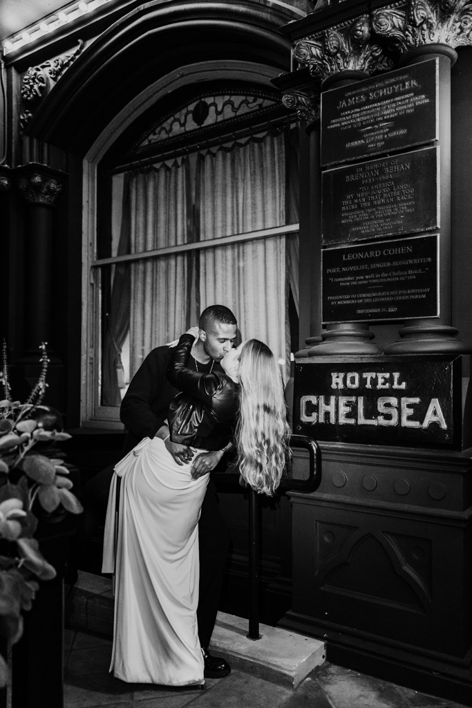Black and white photo of engaged couple kissing outside the Hotel Chelsea at night