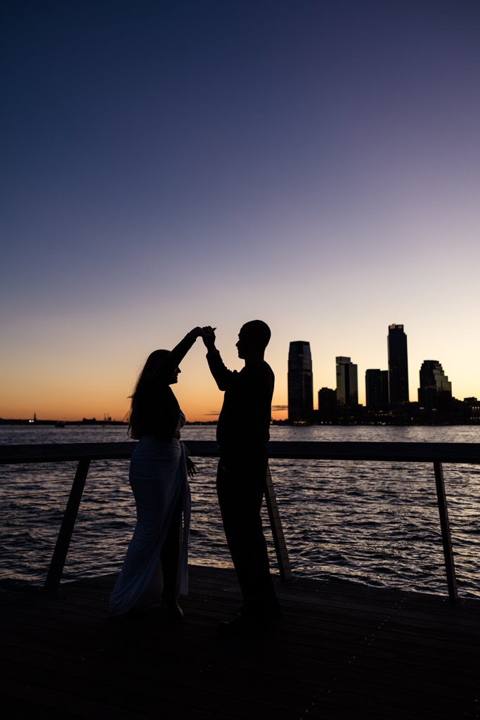 Silhouette of a couple dancing by the water at sunset with the New York City skyline in the background