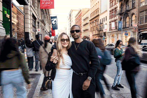 Stylish couple poses on a busy NYC street during their engagement session as people walk by in the background