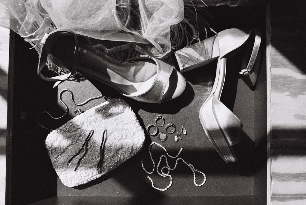 Black and white detail photo of bride's heels, clutch, jewelry, hairpins, and veil arranged on a flat surface for Salvage One wedding