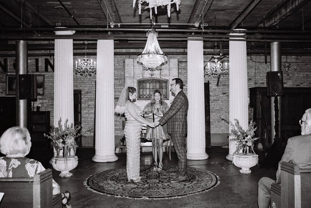 Black and white film photo of bride and groom holding hands during their Salvage One wedding ceremony
