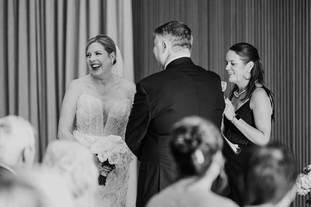 Bride laughing while holding flowers during her Sarabande Chicago wedding ceremony standing with the officiant and groom