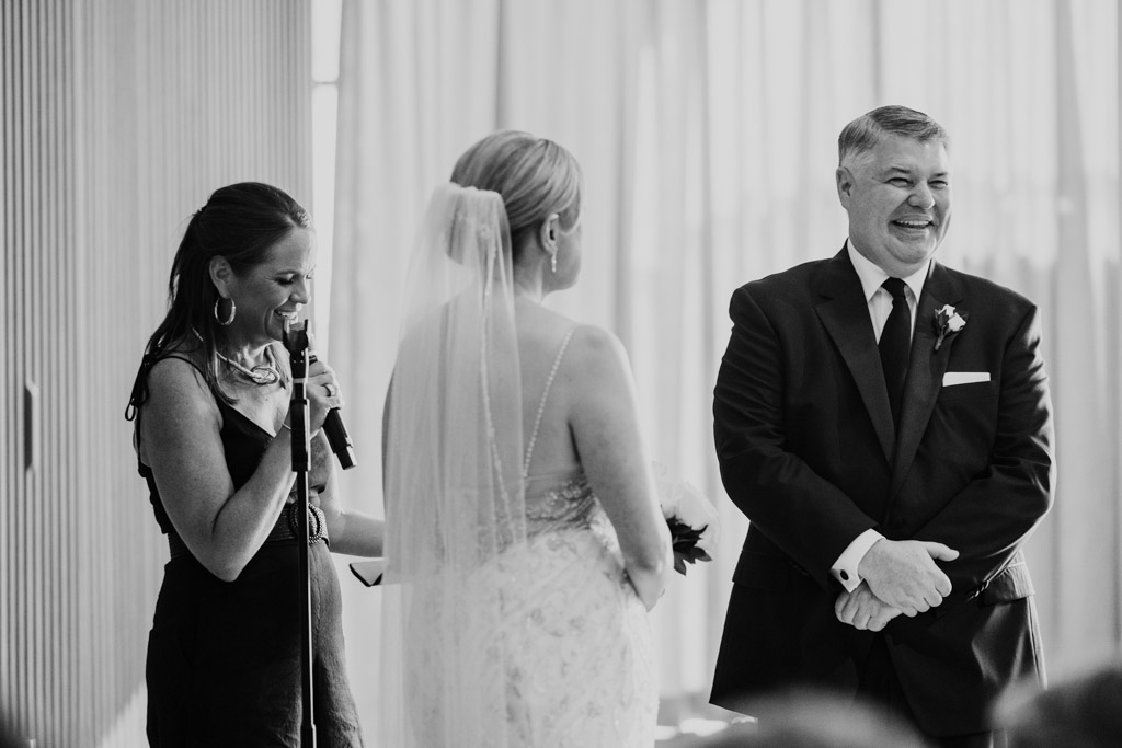 Black and white photo of officiant speaking into a microphone beside bride and groom at their wedding ceremony inside Sarabande Chicago