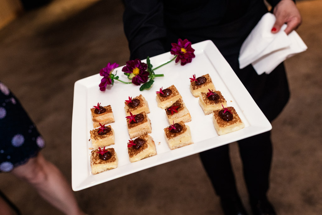 A person holds a tray of appetizers each topped with red garnish and decorated with flowers for wedding reception at Sarabande Chicago