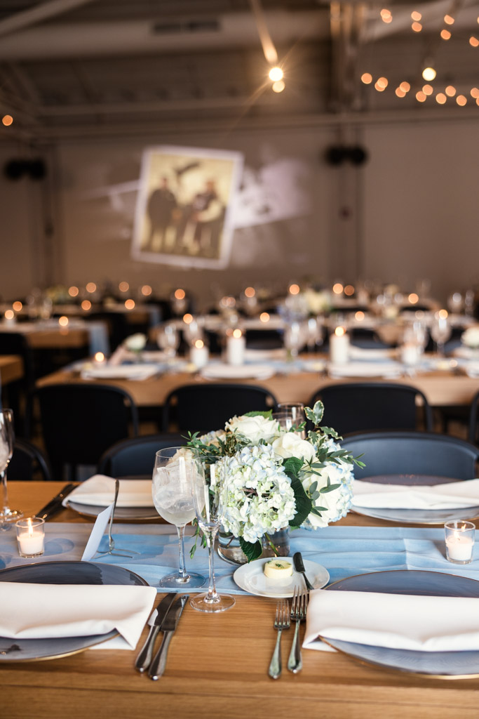 Guest table setting with white flowers, candles, and blue accents for summer wedding reception at Sarabande Chicago