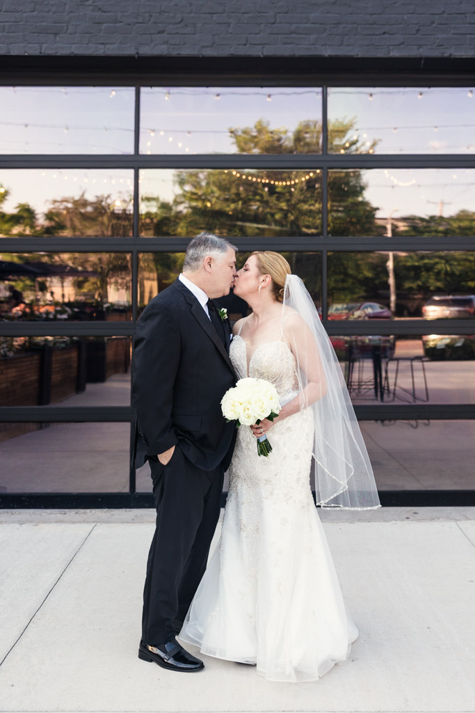 Bride and groom kiss outside Sarabande Chicago, the bride holding a white bouquet