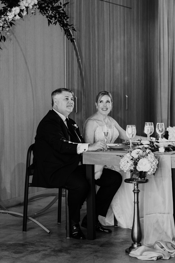 A bride and groom sit at their sweetheart table listening to a speaker during their Sarabande Chicago wedding reception