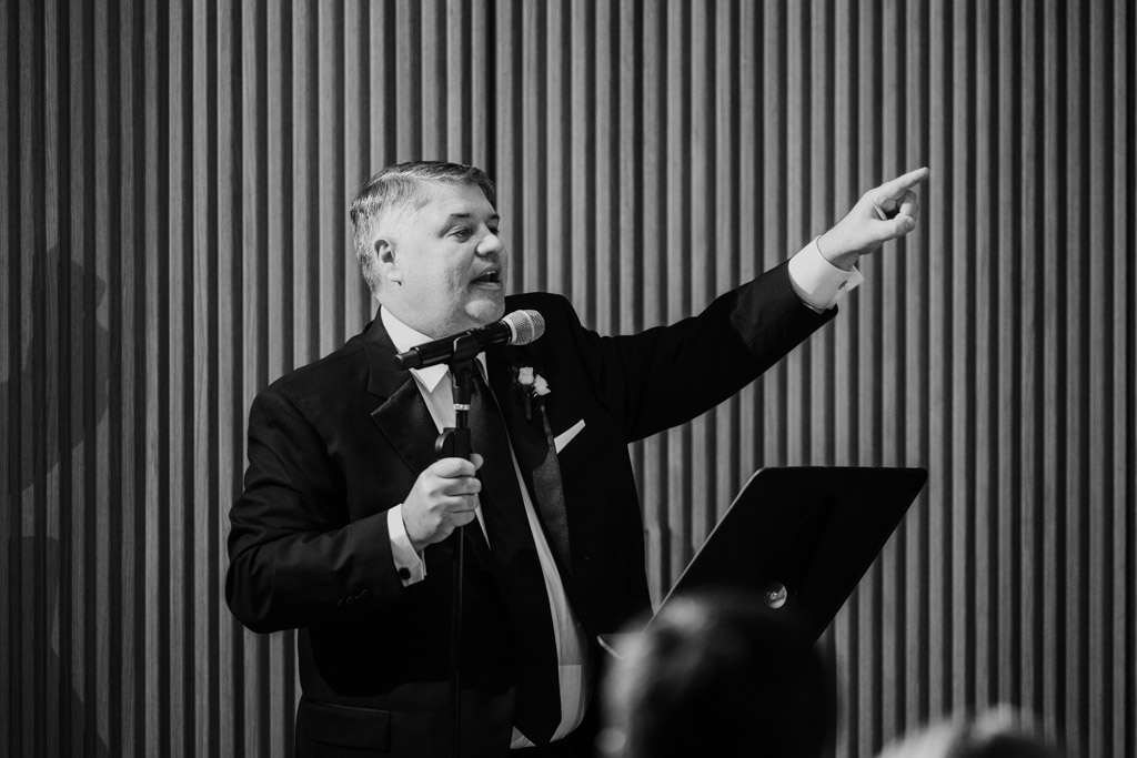 Groom speaking into a microphone and pointing while standing at a podium during wedding reception at Sarabande Chicago