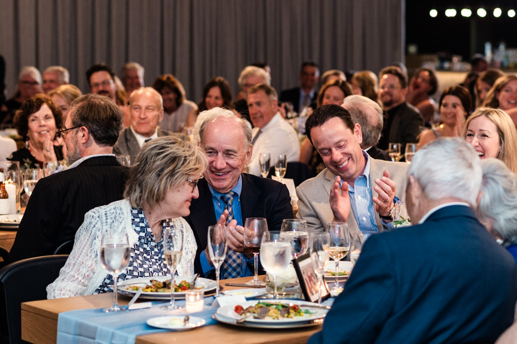 Guests sit at tables, smiling and clapping during wedding reception at Sarabande Chicago