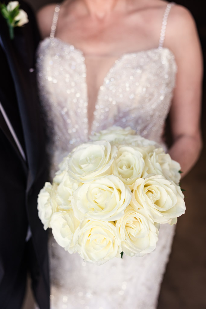 Detail photo of bride's white rose bouquet, held by bride in a white beaded gown