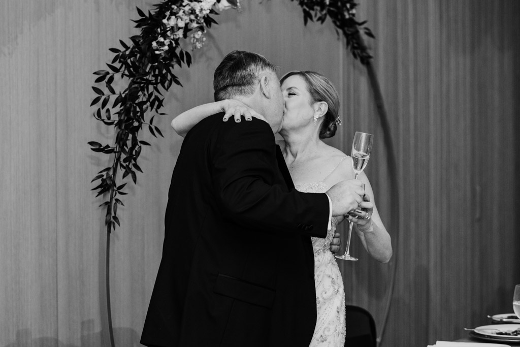 Newlyweds kiss while holding champagne glasses under a floral arch at their Sarabande Chicago wedding celebration