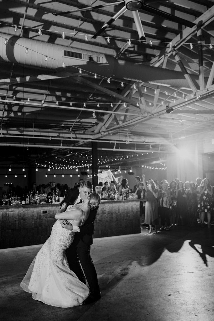 Black and white photo of newlywed couple dipping during their first dance at their Sarabande Chicago wedding reception, surrounded by guests under string lights