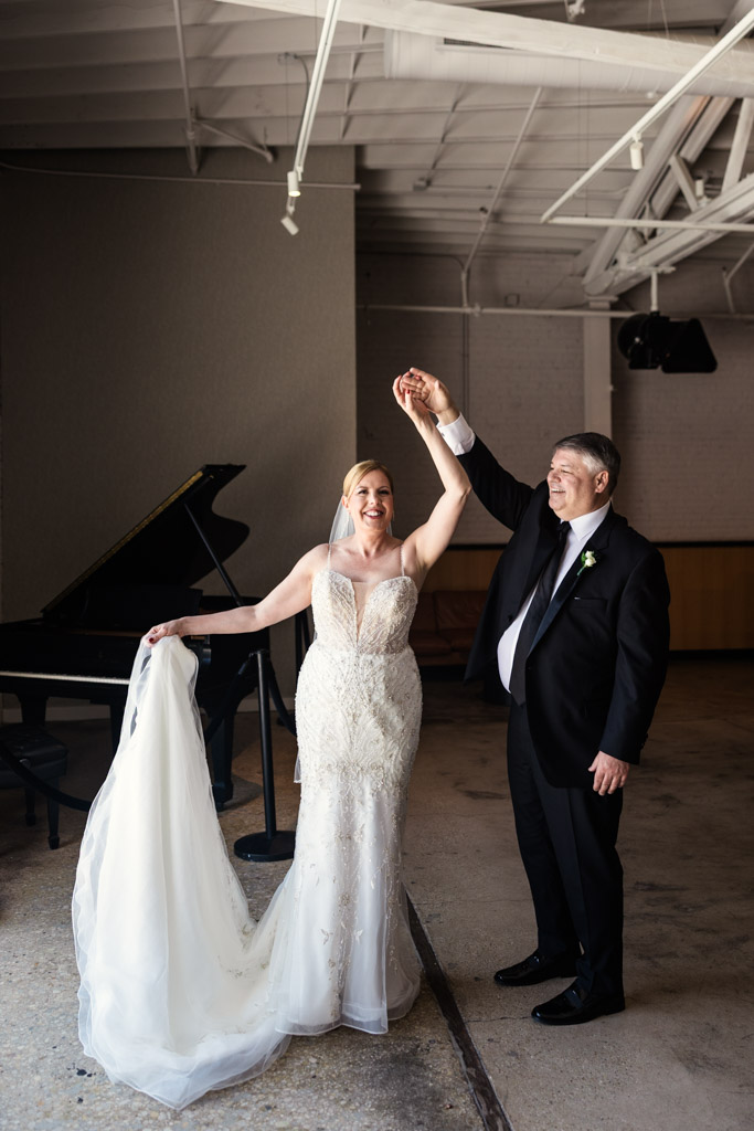 Happy bride and groom dance near a grand piano, holding hands and dressed in elegant wedding attire before their Sarabande Chicago wedding celebration