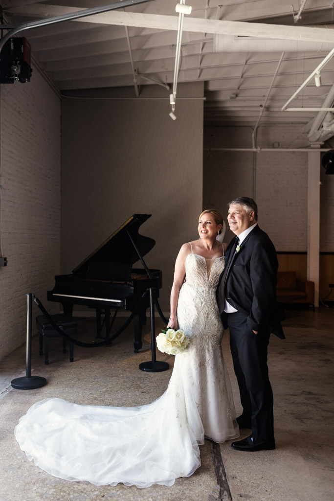 Bride and groom smiling indoors beside a black grand piano, with sunlight streaming in at Sarabande Chicago