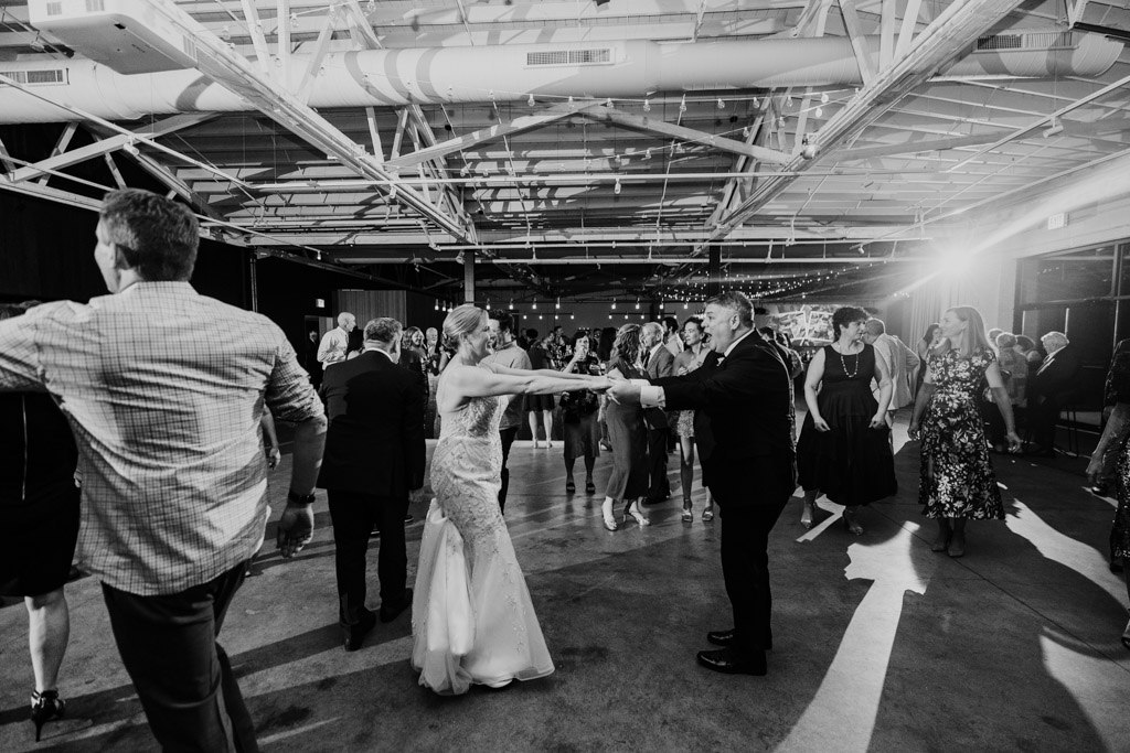 Black and white photo of bride and groom dancing joyfully during their festively lit indoor wedding reception at Sarabande Chicago