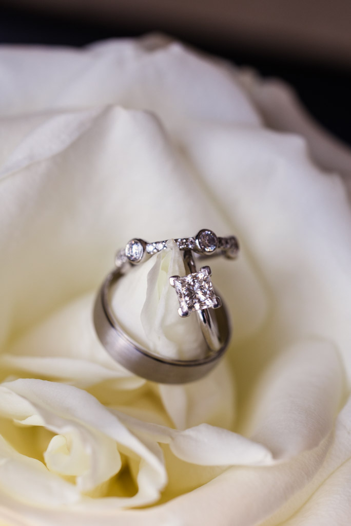 Two wedding rings and an engagement ring rest on a white rose for wedding celebration at Sarabande Chicago