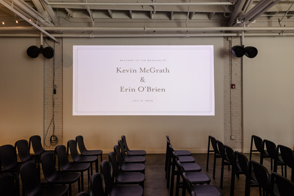 Rows of black chairs beneath a projected wedding welcome sign for wedding celebration at Sarabande Chicago