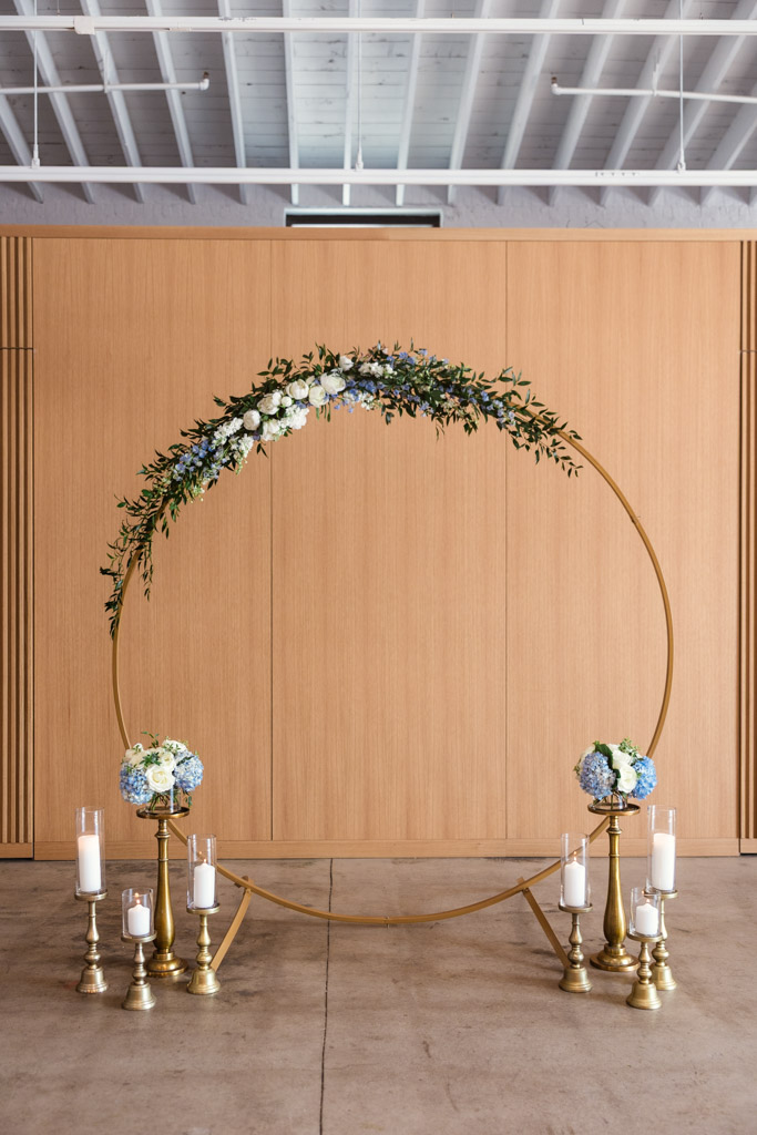 A gold circular wedding arch with blue and white flowers, candles, and gold for summer wedding ceremony at Sarabande Chicago