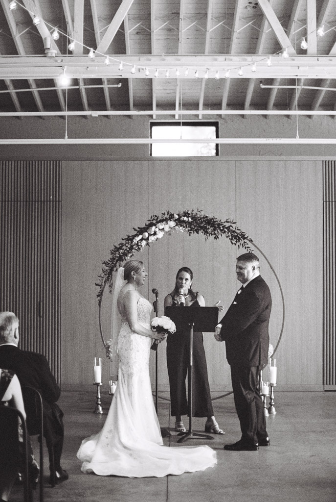 Bride and groom stand before an officiant under a floral arch during their indoor wedding ceremony at Sarabande Chicago