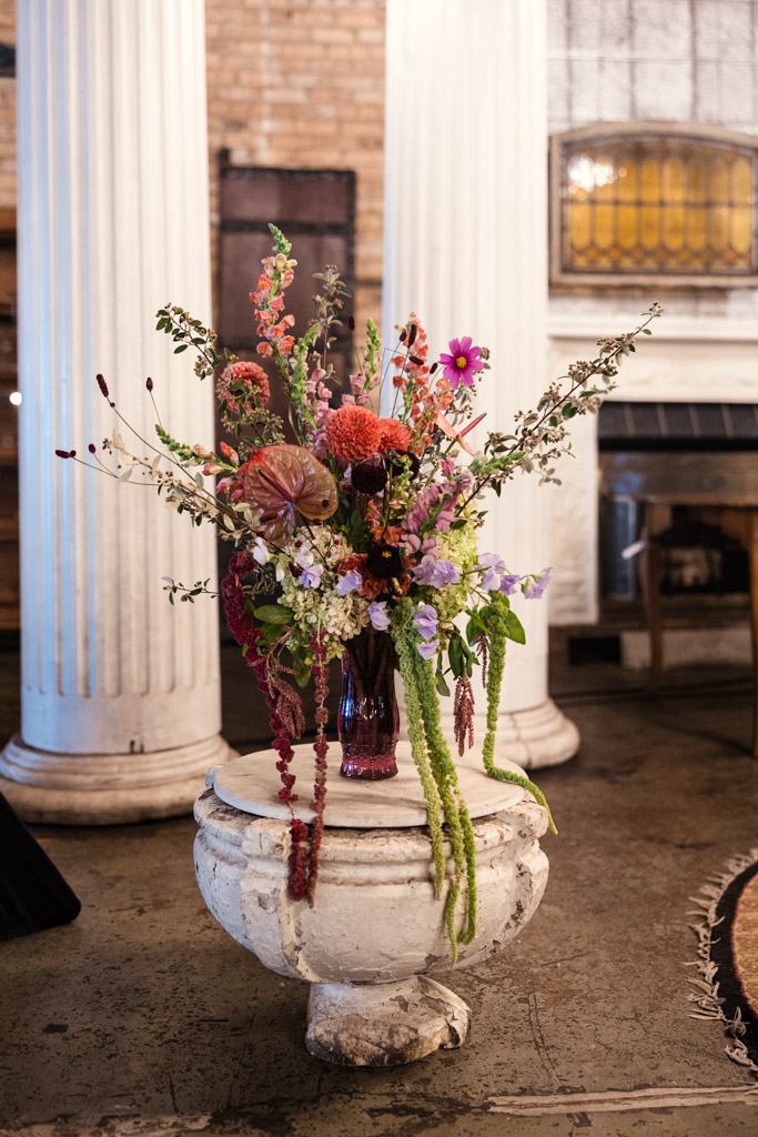 A colorful floral arrangement in a vase sits on a white pedestal between two large columns inside the Salvage One wedding ceremony space