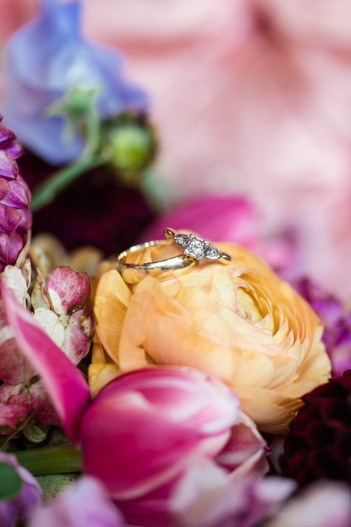 Detail photo of two gold rings with diamonds resting on a yellow flower in the bride's bouquet for Salvage One wedding celebration