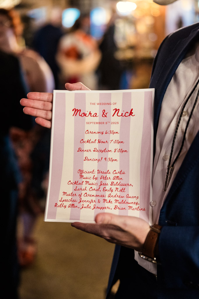A person holds a pink and white striped wedding program for Salvage One wedding celebration