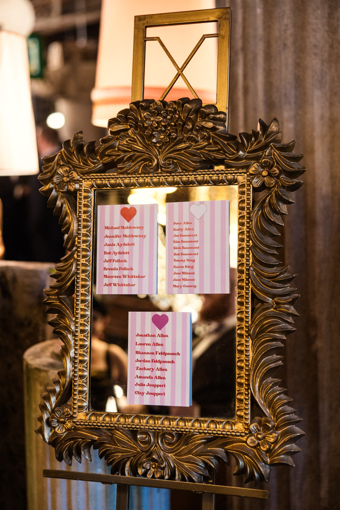 Ornate gold-framed mirror displaying wedding seating cards with guest names and red heart decorations for Salvage One wedding celebration
