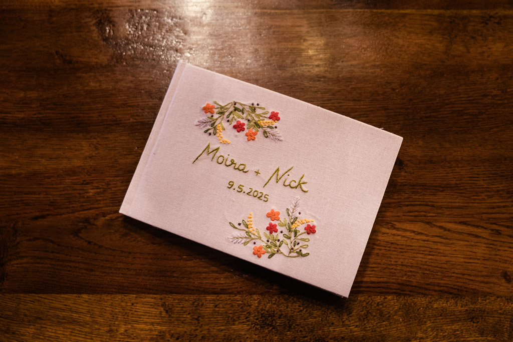 A pink wedding guest book with floral designs rests on a wooden table for Salvage One wedding