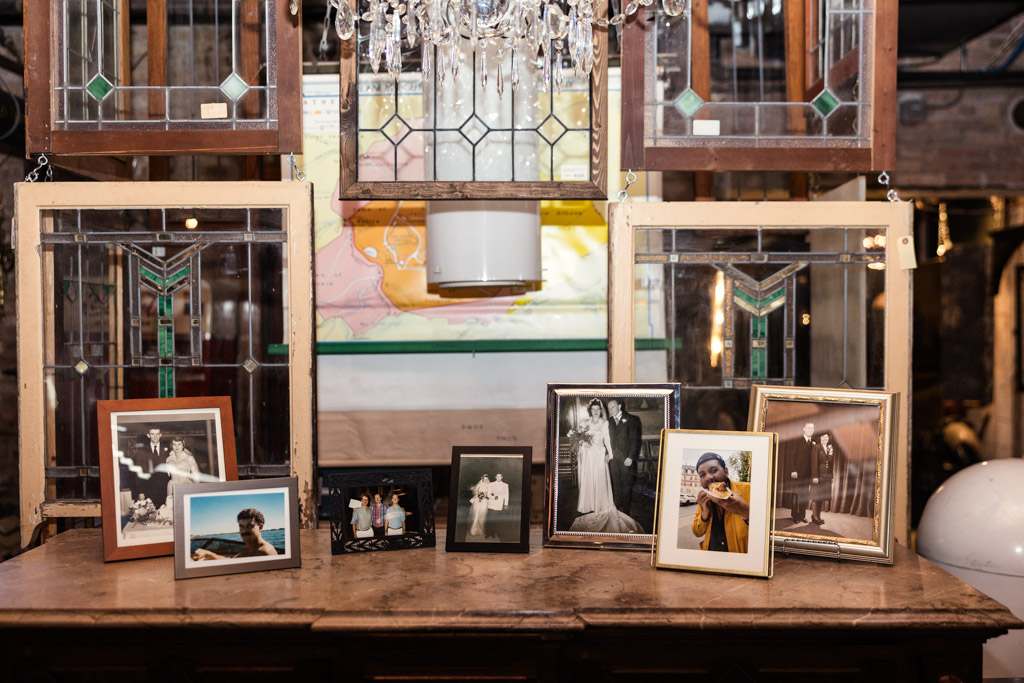 Memory table displays framed family photos in front of stained glass windows with a chandelier above for Salvage One wedding