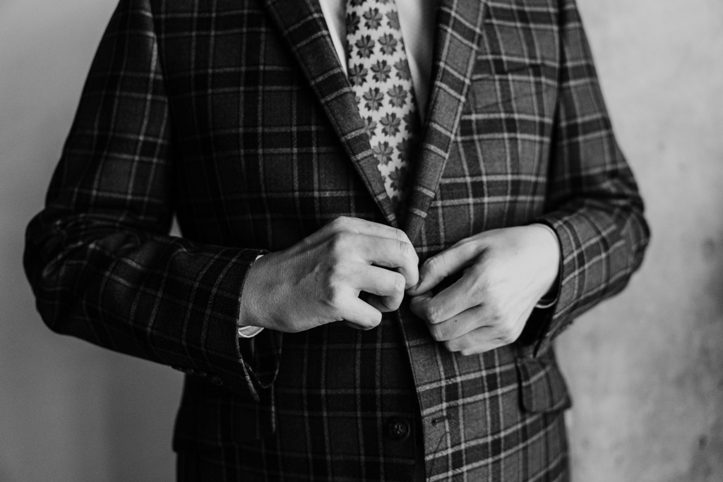 Black and white photo of groom buttoning his plaid suit jacket as he gets ready at the Emily Hotel in Chicago